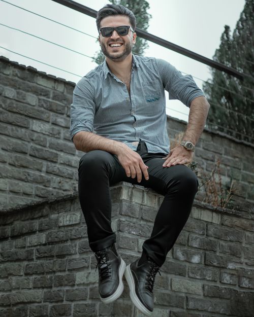 Free Trendy man in sunglasses smiling and sitting on a wall in an urban setting. Stock Photo
