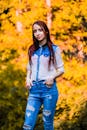 一位身着牛仔的年轻女子，自信地站在秋叶生机勃勃的景色中，散发着时尚与魅力