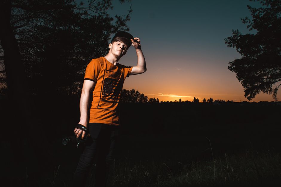 Portrait of a young man standing outdoors in a rural field during sunset, creating a dramatic silhouette.