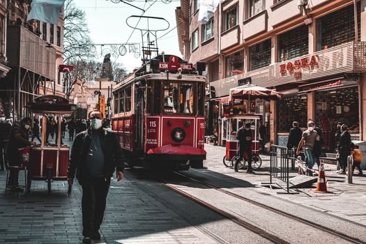 Iconic red tram traverses a lively Istanbul street, bustling with people and shops.