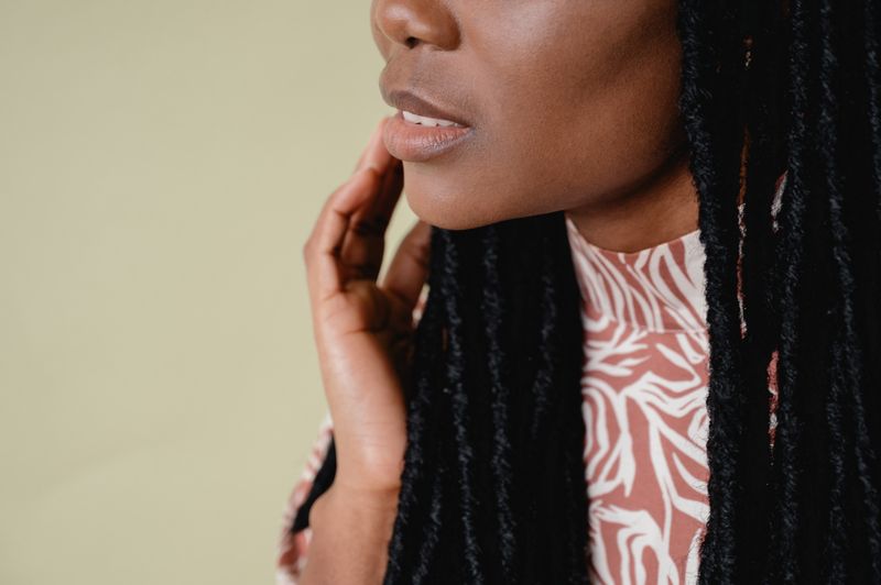 A Black woman with long locs rests her hand against her cheek, just below her lips.