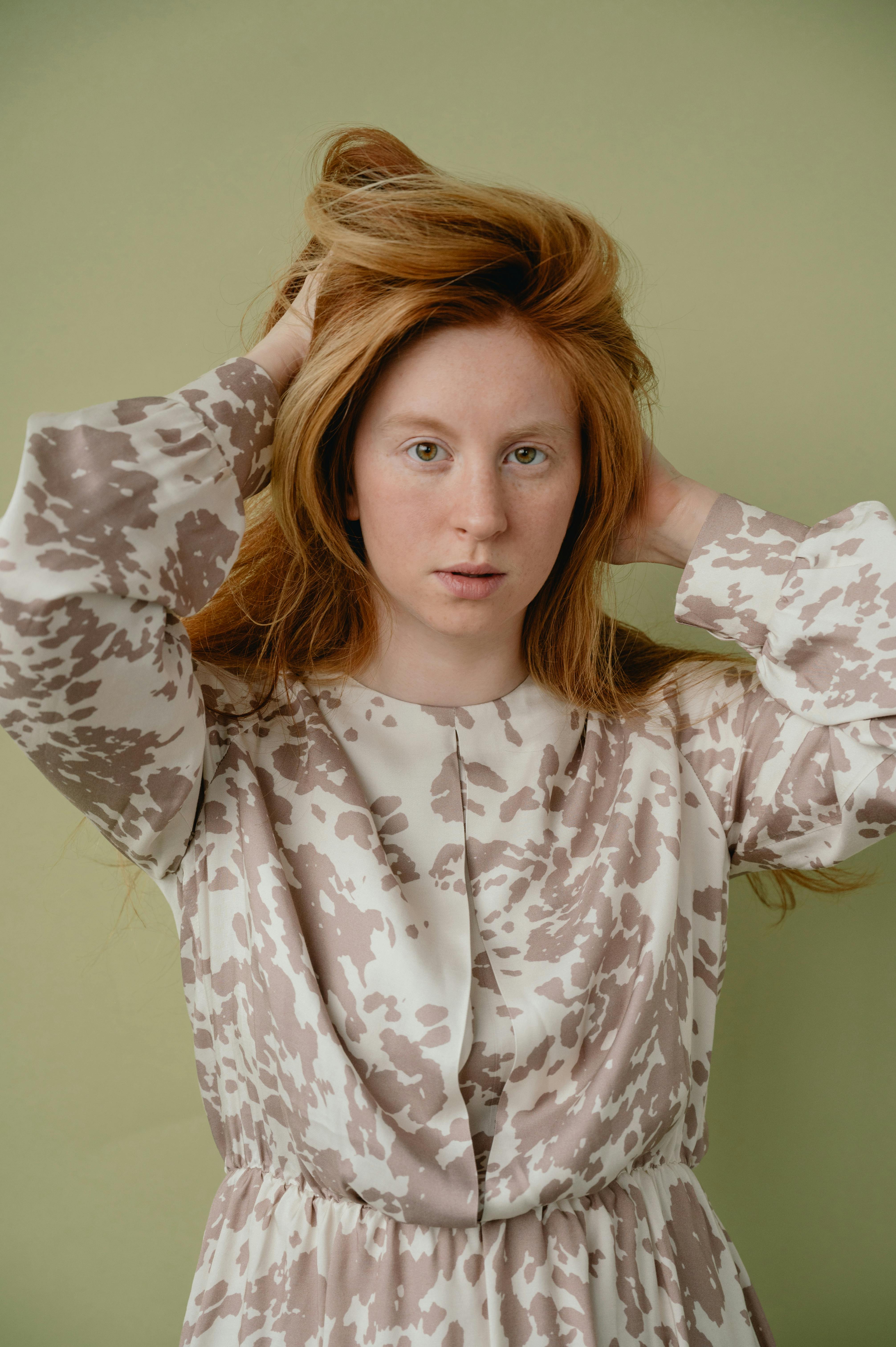 Elegant portrait of a young woman in a stylish patterned dress against a light green background.