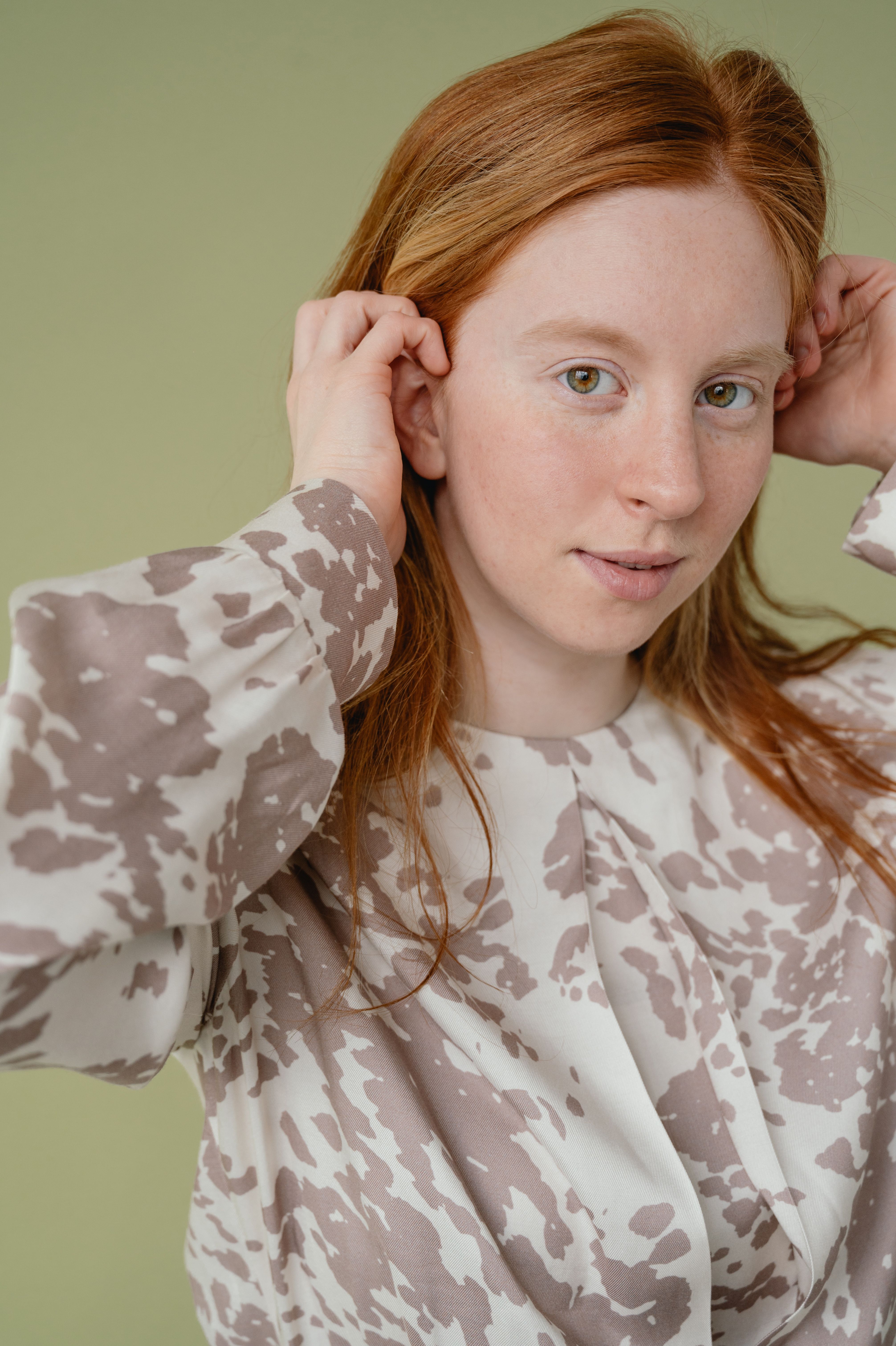 Close-up of a young woman with red hair wearing a stylish patterned blouse indoors.