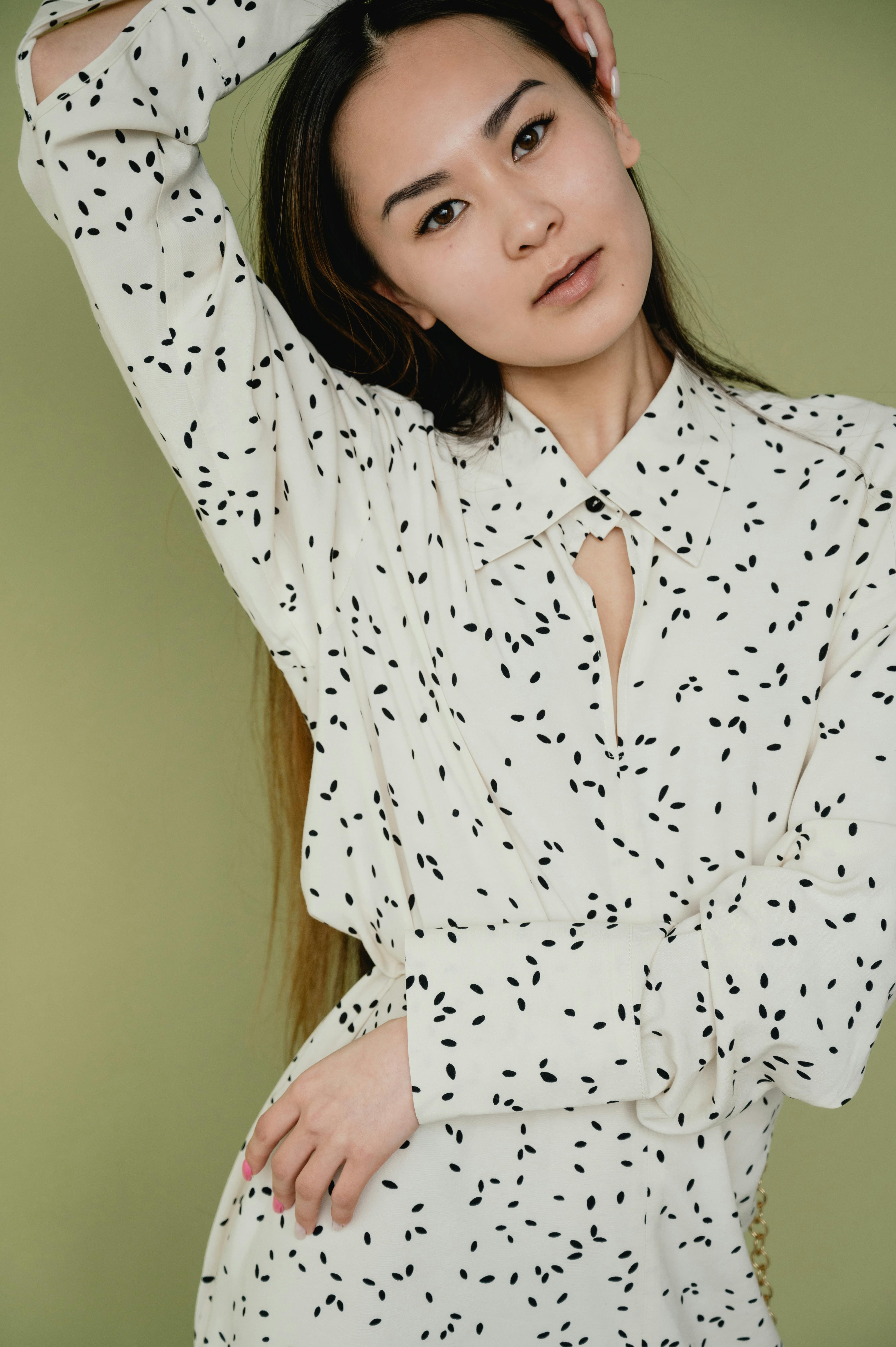 Asian woman posing in a white patterned dress against a green background.