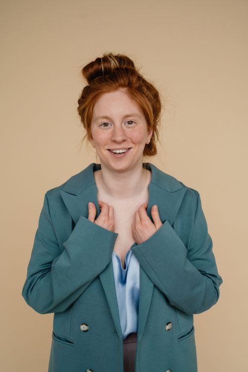 Free Portrait of a stylish young woman with red hair in a teal blazer, smiling warmly. Stock Photo