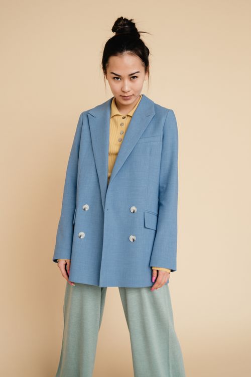 Free Portrait of a woman in a blue blazer and green pants against a neutral background, showcasing modern fashion. Stock Photo