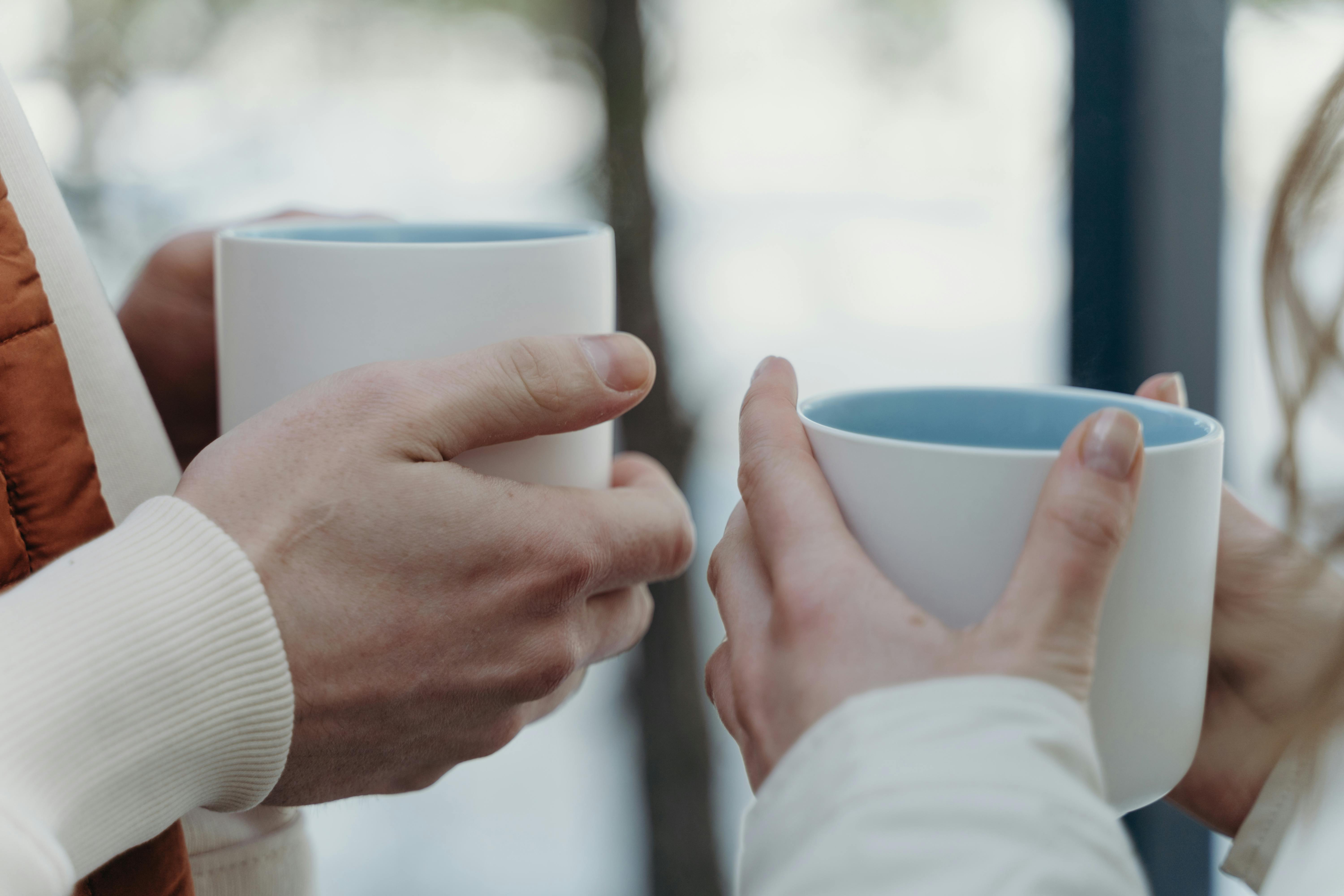 Close-up of hands holding ceramic mugs filled with warm drinks, evoking a cozy atmosphere.