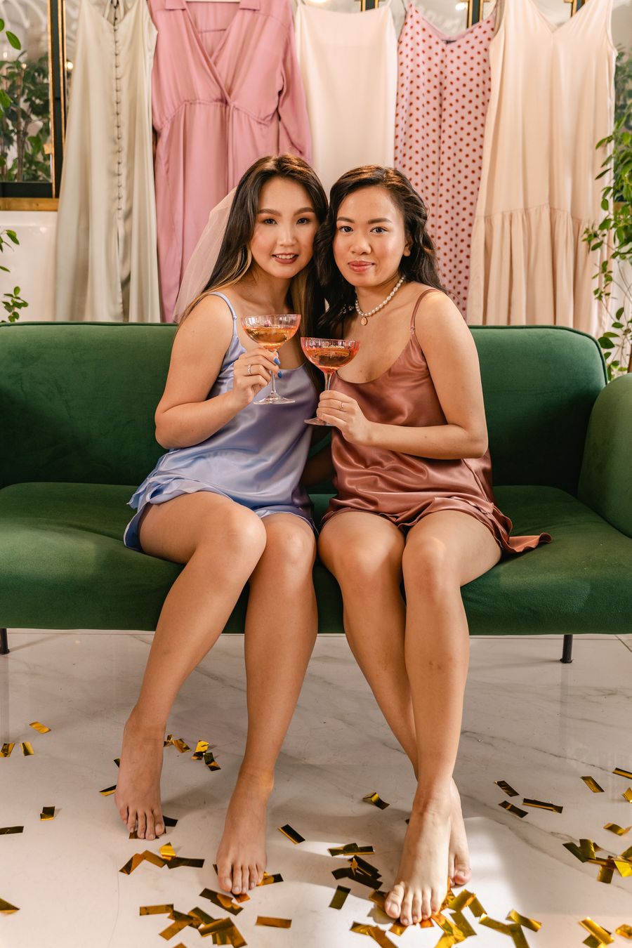 Three friends in satin dresses celebrating with confetti and drinks