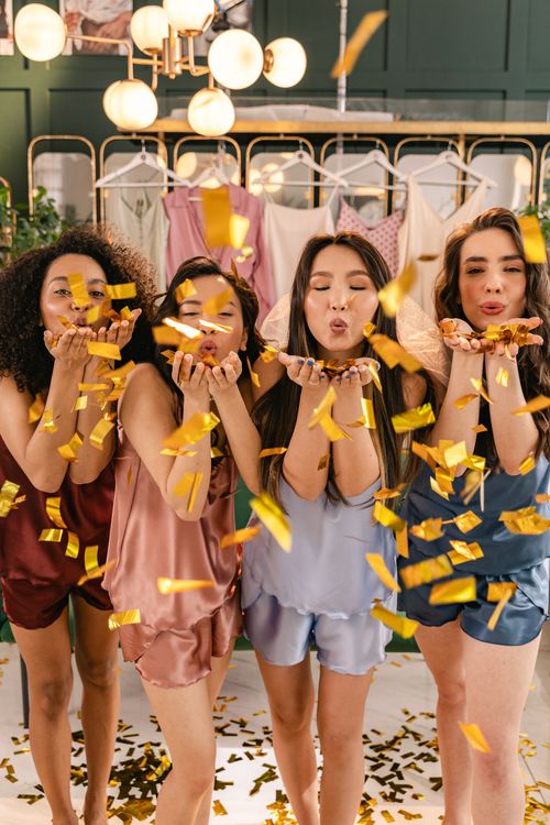 Free Four women in stylish nightwear joyfully celebrating with confetti indoors. Stock Photo