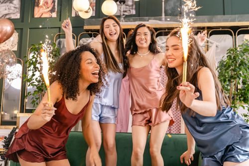 Free Group of young women celebrating indoors with sparklers, wearing colorful sleepwear, enjoying a joyful moment. Stock Photo