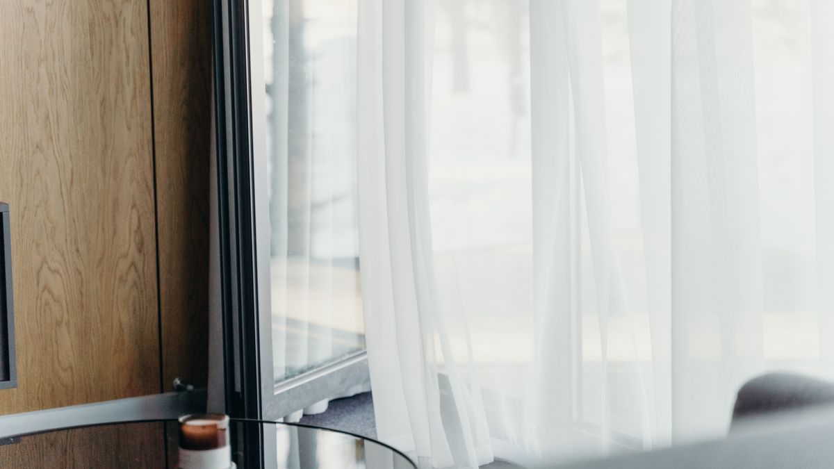 A softly lit modern hotel room with sheer curtains and a made bed