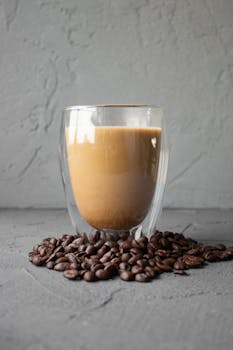 Elegant double-walled glass filled with coffee surrounded by coffee beans on gray textured surface.
