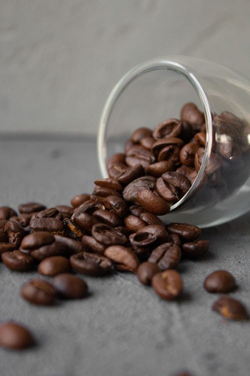 Free Overturned glass filled with roasted coffee beans on a grey surface. Stock Photo