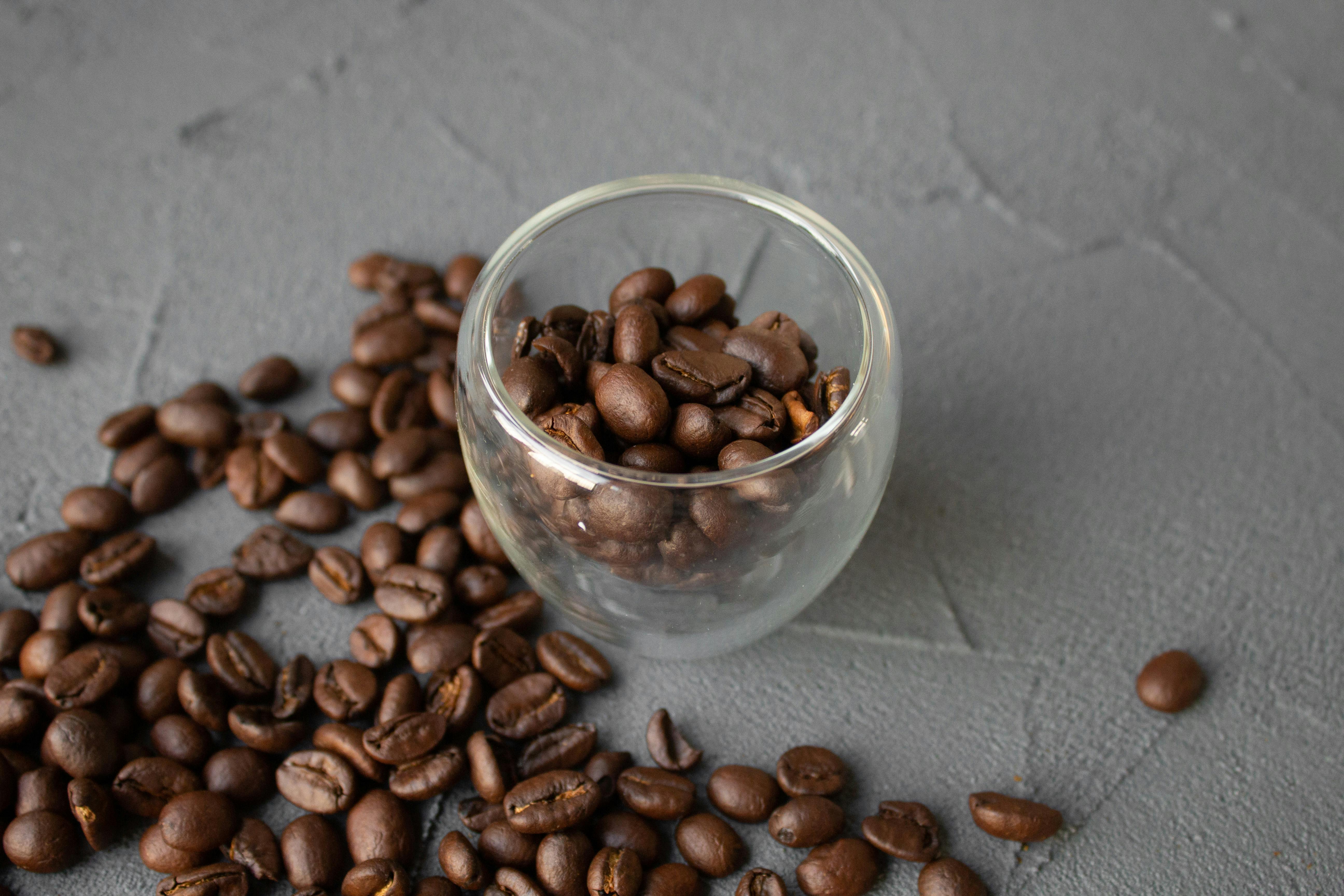 From above of fragrant coffee beans scattered near glass cup on gray uneven surface in daylight