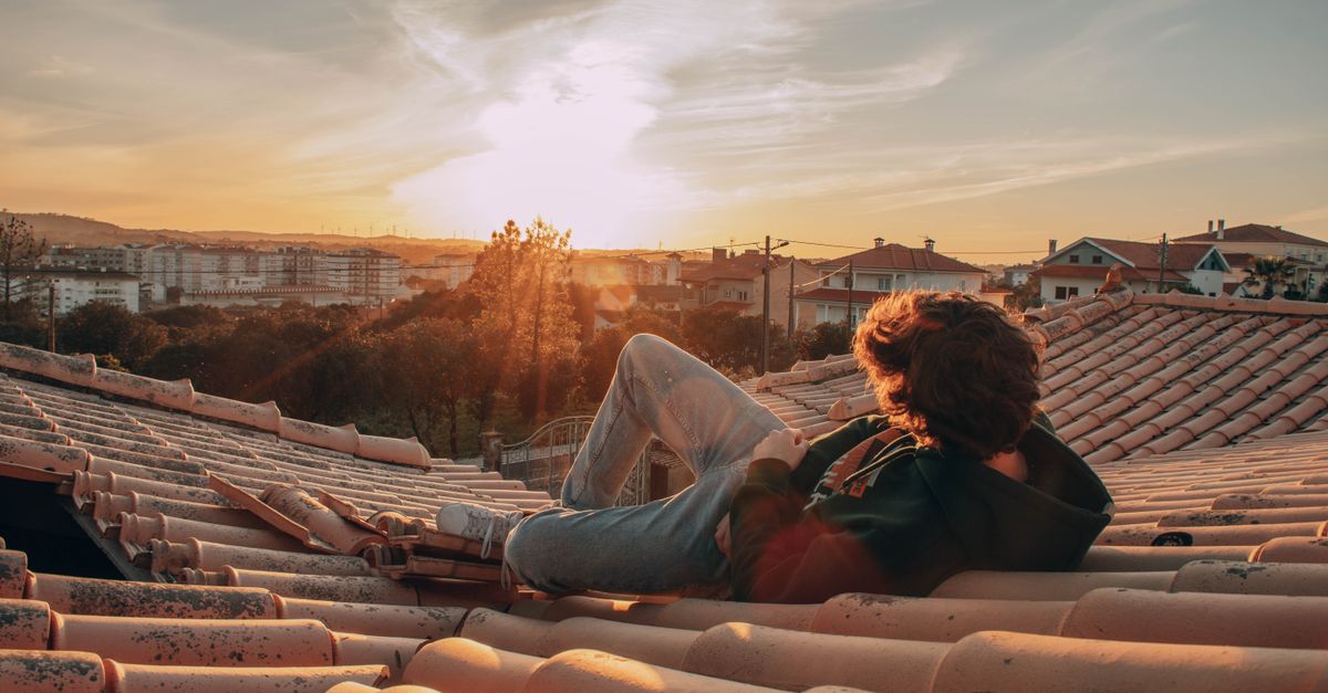 traveler sitting on a rooftop in a foreign city, looking at a sunset with a local person