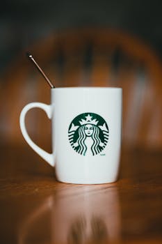Close-up of a white mug with a logo, placed on a wooden table, featuring a spoon.