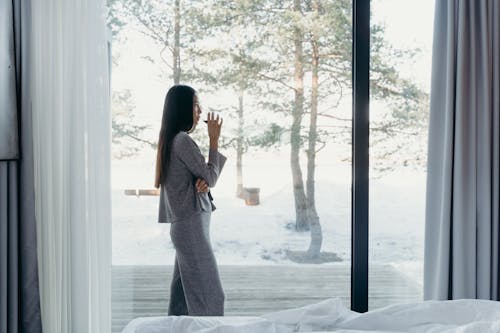 Woman in Gray Long Sleeves and Pants Standing Near a Glass Window