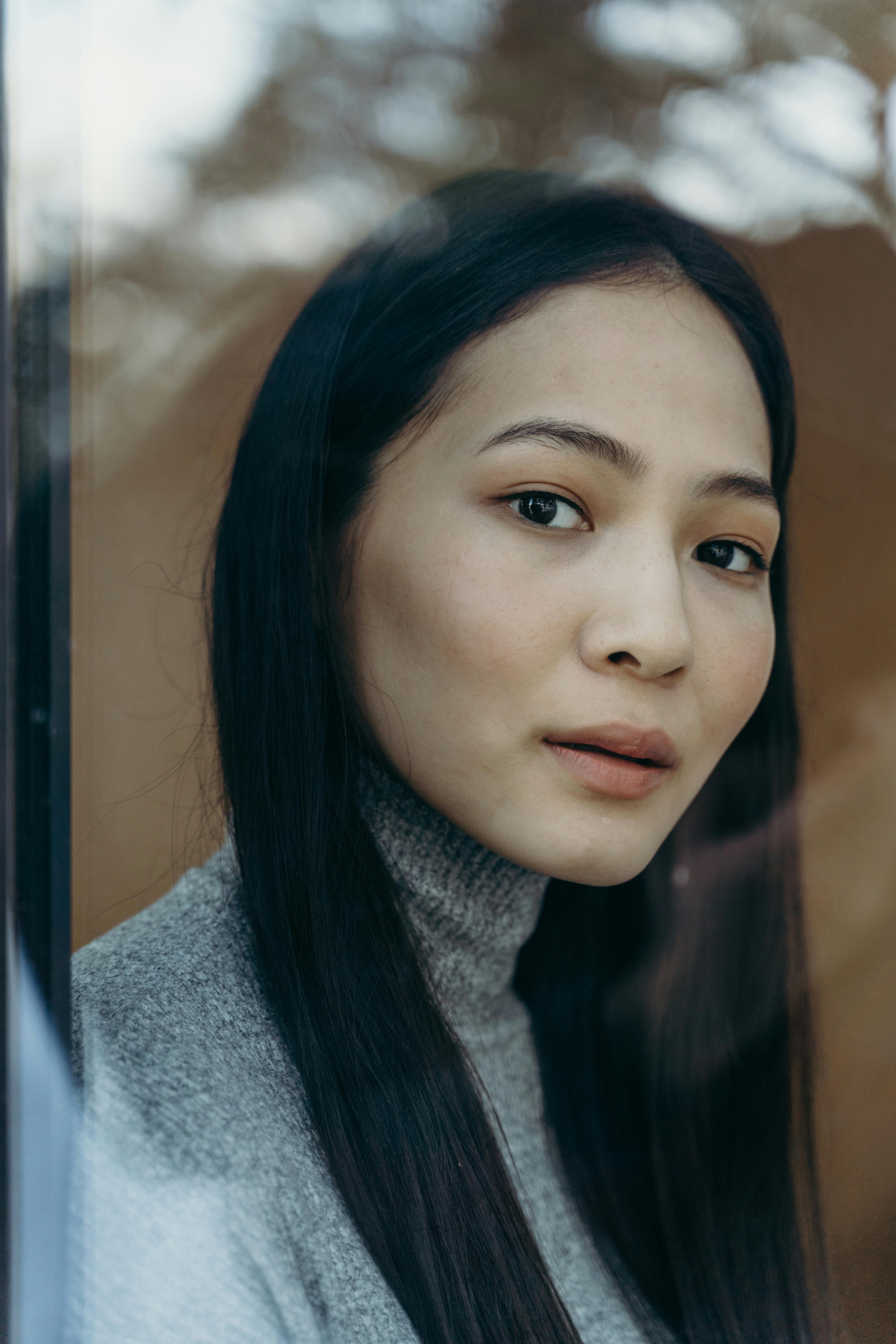 Close-up portrait of a woman gazing through a window, combining natural light and reflection.