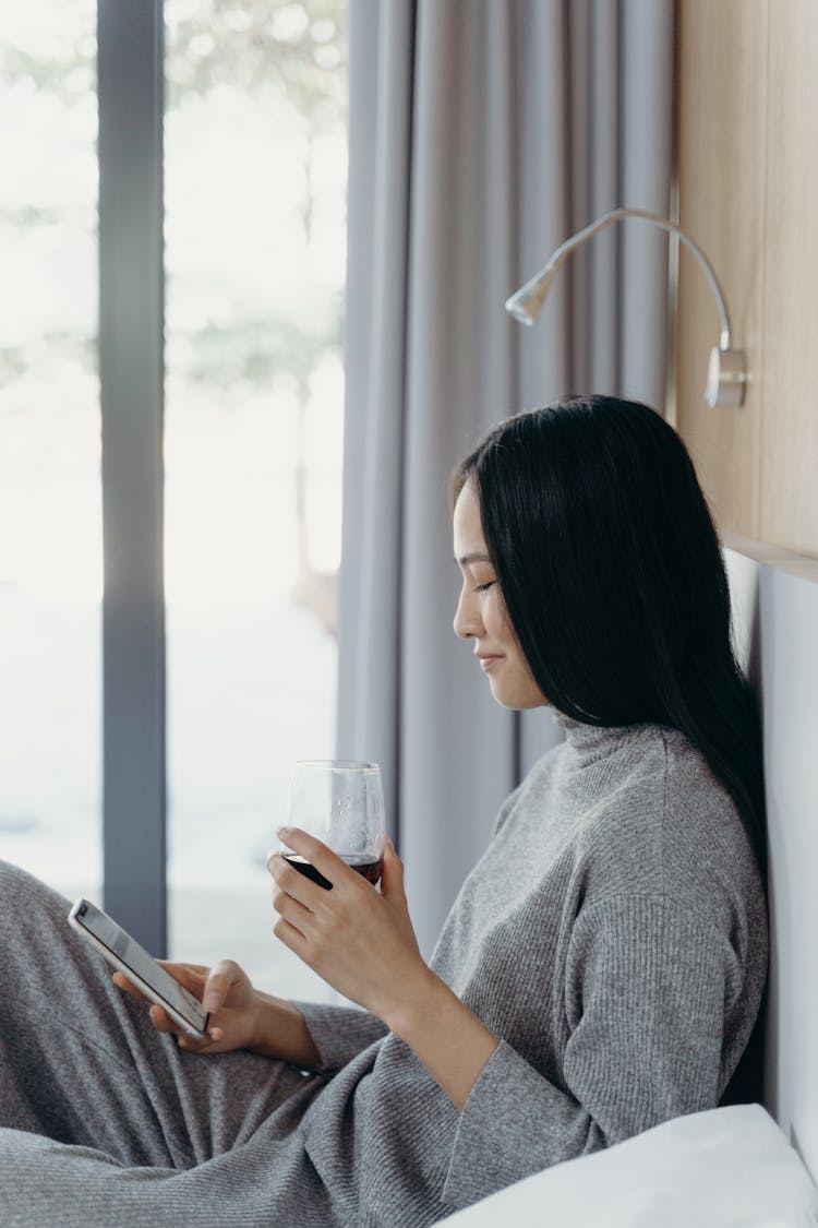 A Happy Woman In A Gray Outfit Using A Smartphone