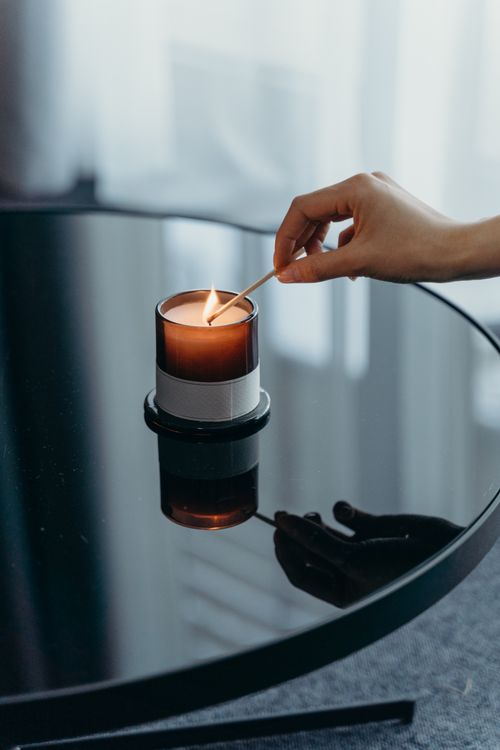 Free Close-up of a hand lighting a candle on a shiny table, creating a warm ambiance. Stock Photo