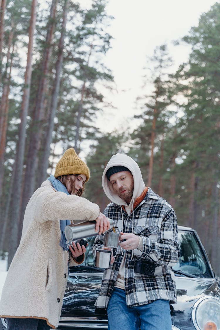 A Couple In Winter Clothes Having Coffee In Front Of A Car