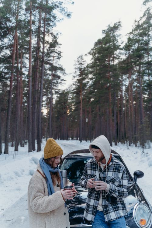 Free A couple enjoys hot tea outside their car in a snowy forest setting. Stock Photo
