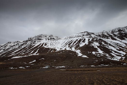 Scenic view of snow-covered mountains under a gray sky in Búðardalur, Iceland.