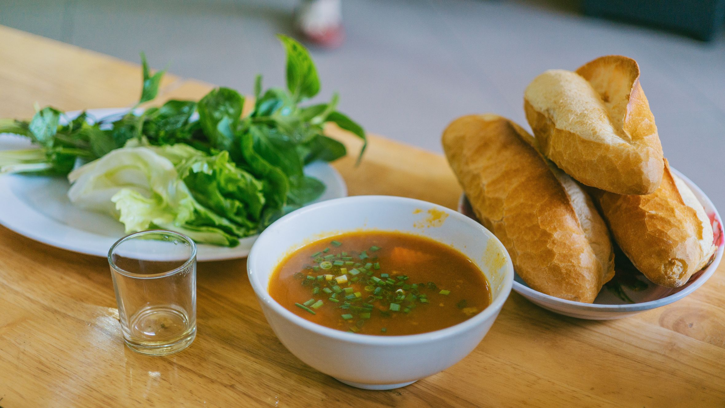 A bowl of flavorful Vietnamese soup accompanied by fresh greens and crusty baguette.