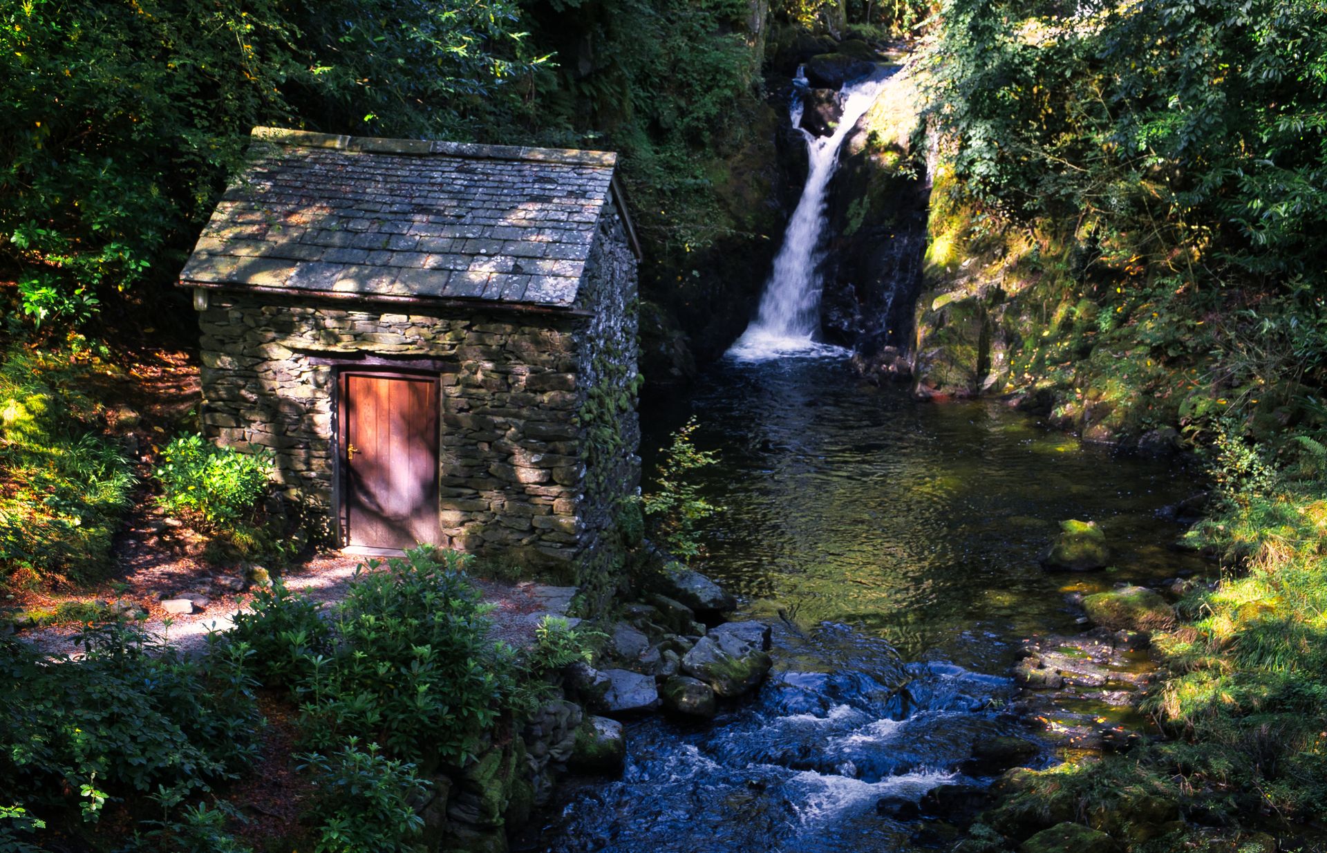 A charming stone house by a woodland waterfall captures the serene beauty of English nature.