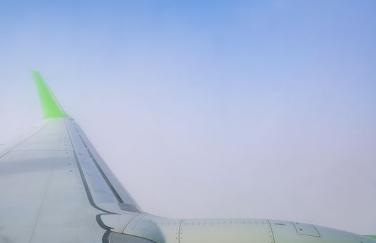 Airplane wing view from the window with a vibrant green tip against a clear blue sky.