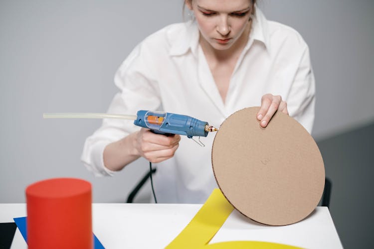 A Woman Using A Glue Gun On Cardboard