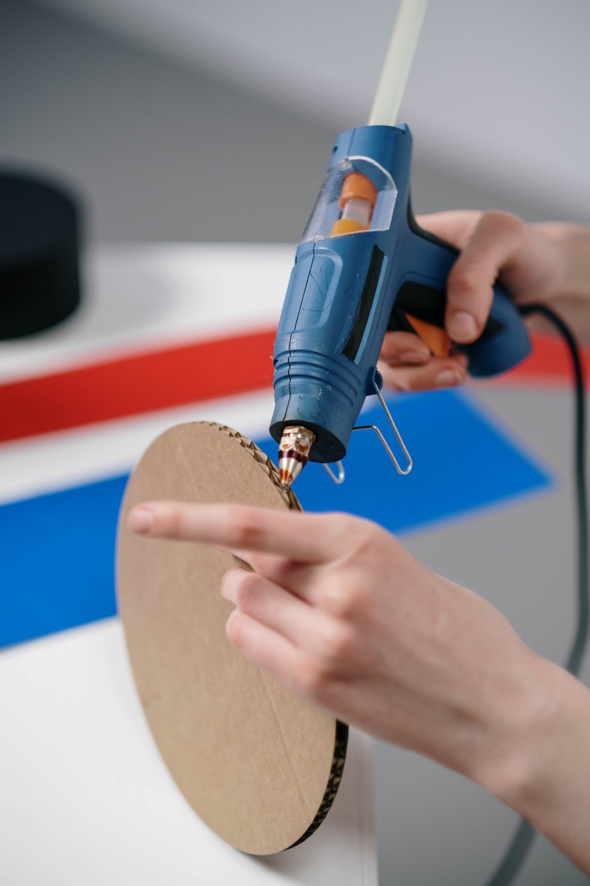 Hands building a cardboard desk organizer with a hot glue gun