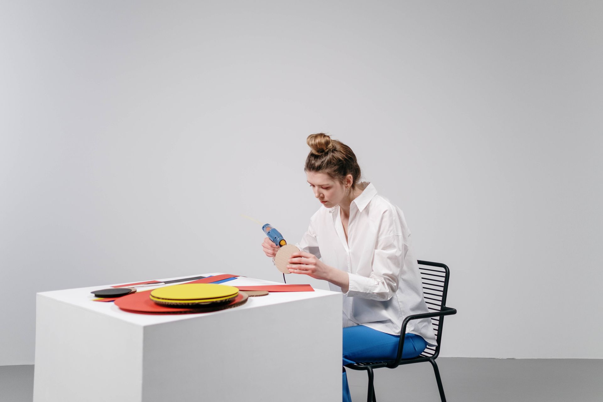Artist working on a craft project at a desk using a glue gun, showcasing creativity and focus.