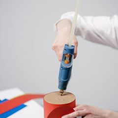 A blue mini glue gun held upright over a red paper craft