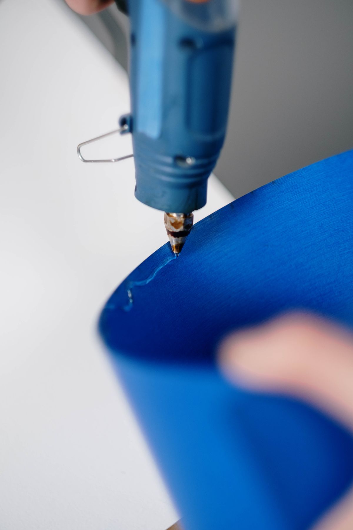 Glue gun applying dimensional hot glue dots and lines on blue paper