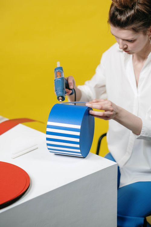 Free Caucasian woman focusing on arts and crafts using a glue gun on cardboard with a yellow background. Stock Photo