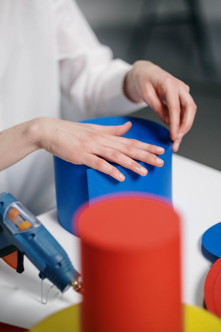 Person Resting Hands On A Blue Round Carton 