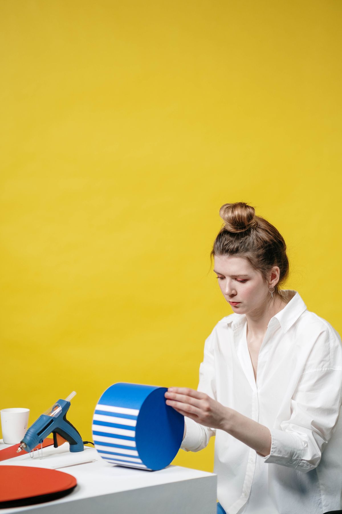 Woman embellishing a gift box with a glue gun against a yellow background