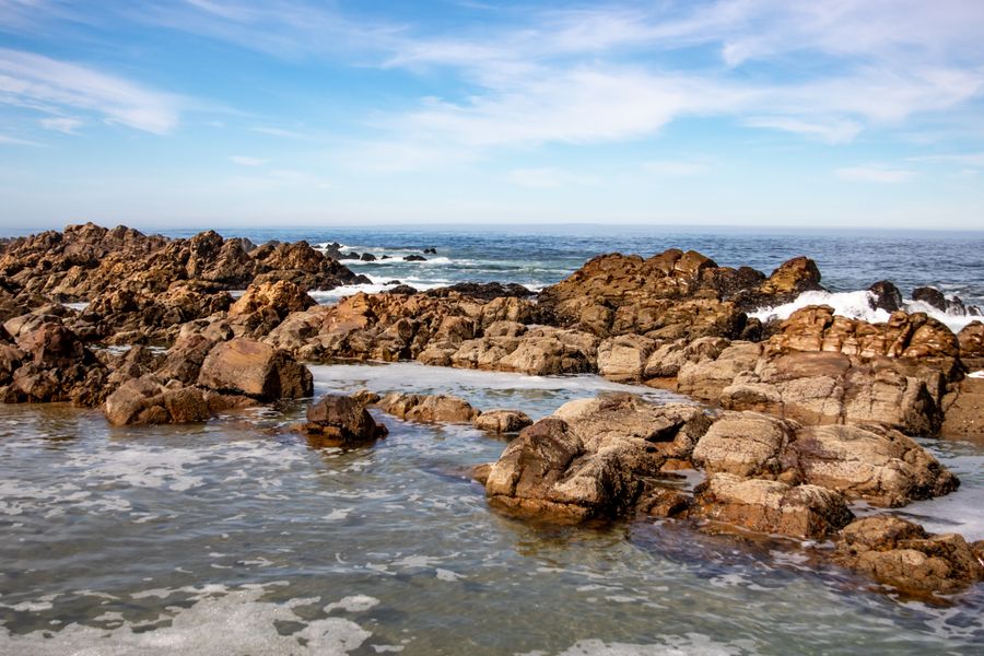 A scenic view of rocky coast with ocean waves and a clear blue sky.