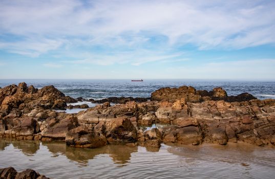 A peaceful ocean view with rock formations and a ship on the horizon under a blue sky.