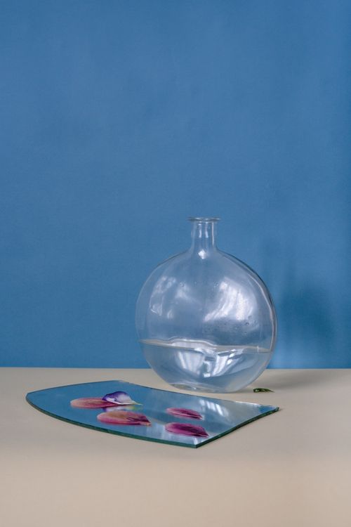 Free Artistic still life of a water-filled glass bottle beside a broken mirror with flower petals. Stock Photo
