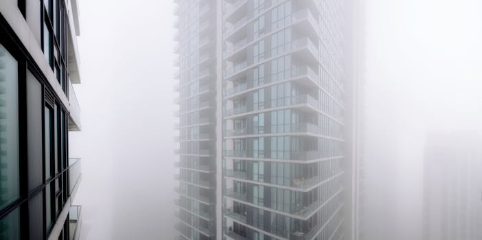 Contemporary residential building with balconies covered with thick fog located on street of modern city with houses in overcast weather