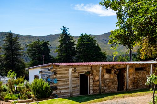 Free A peaceful rural scene featuring a rustic wooden cabin surrounded by lush greenery and distant mountains. Stock Photo