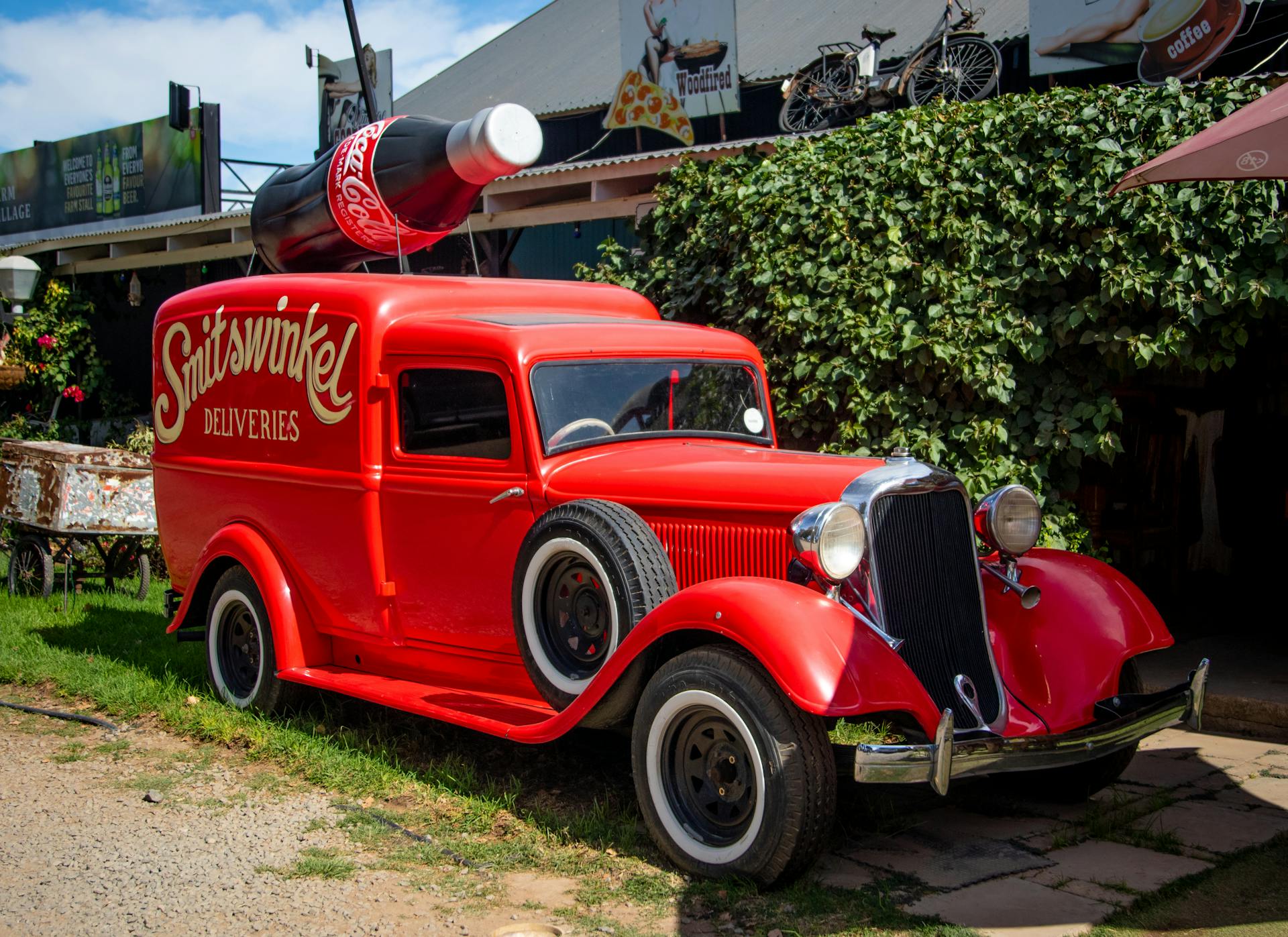 Classic red vintage delivery truck with a giant Coca-Cola bottle on top parked outdoors.