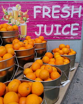 Bright orange oranges in metal buckets near a fresh juice sign, ideal for healthy food themes.