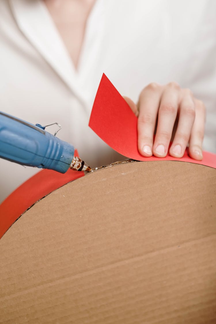 Person Sticking Paper On Cardboard Using A Glue Gun