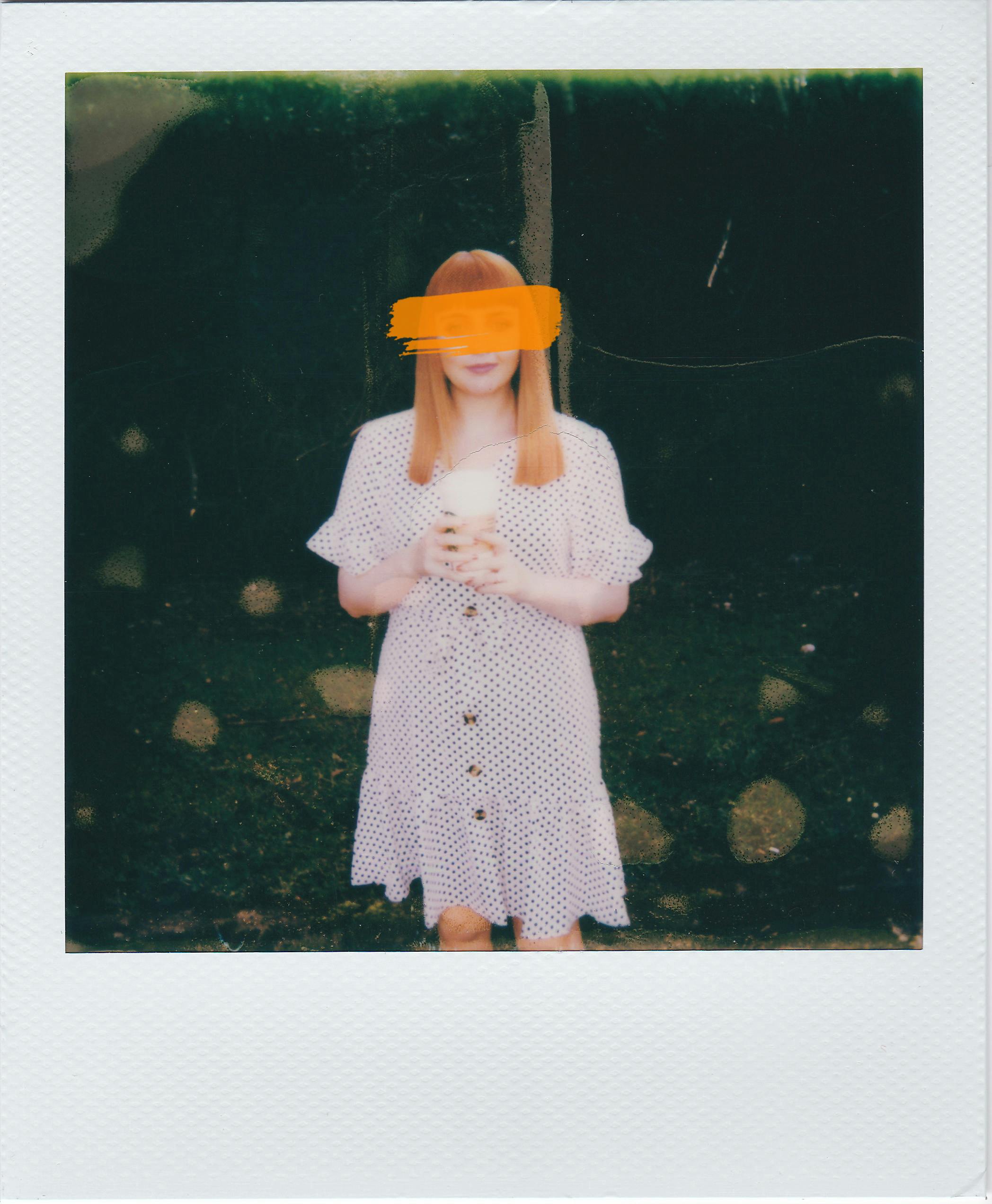 Vintage Polaroid of a red-haired woman in a polka dot dress holding a cup.