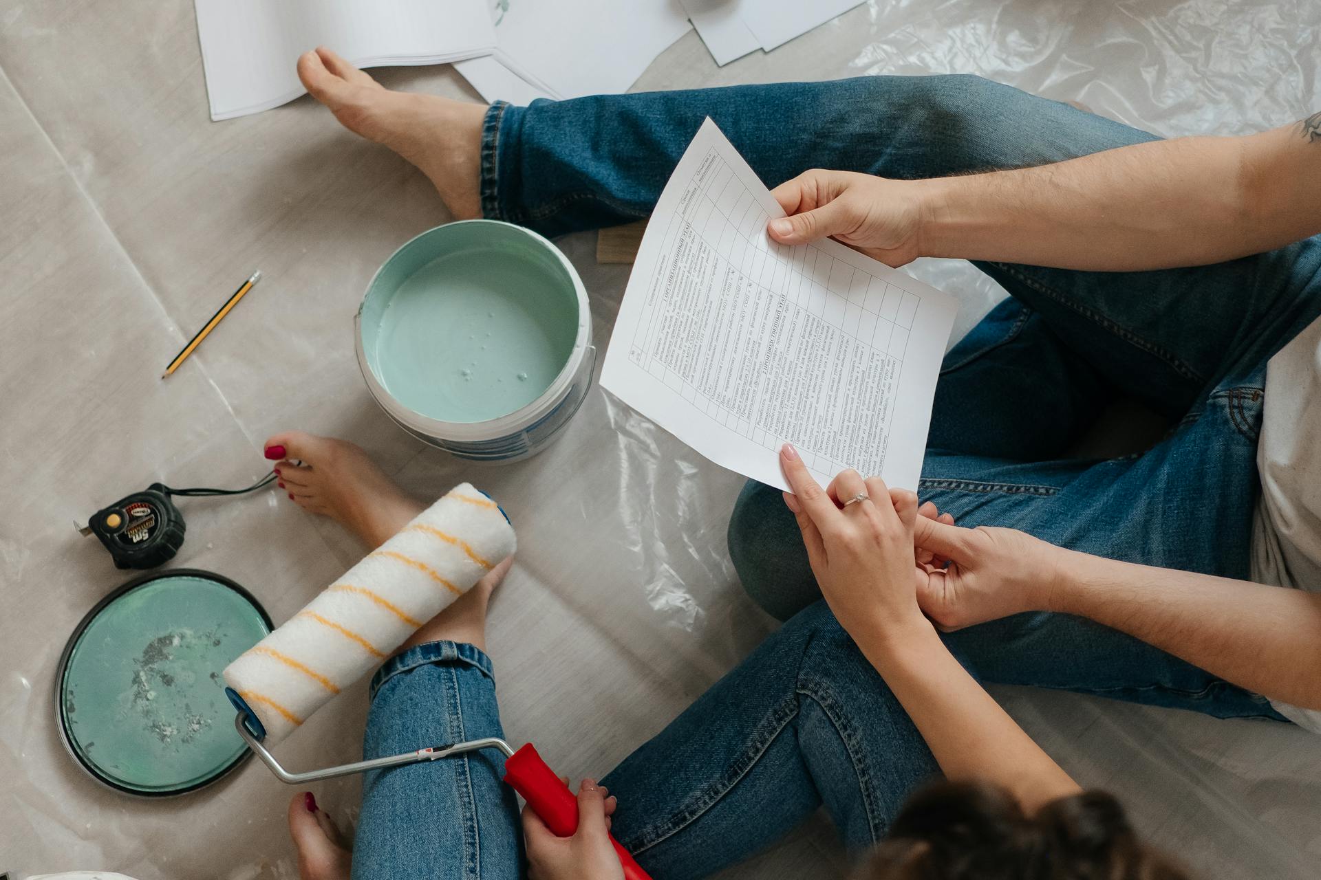 A couple sitting on the floor planning home renovation with paint, documents, and tools.