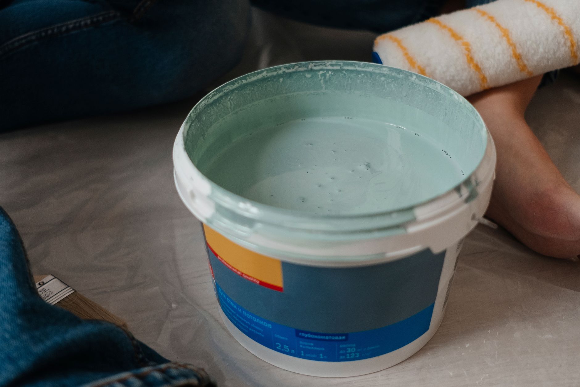 A close-up view of a bucket filled with mint green paint and a paint roller, perfect for home renovation projects.