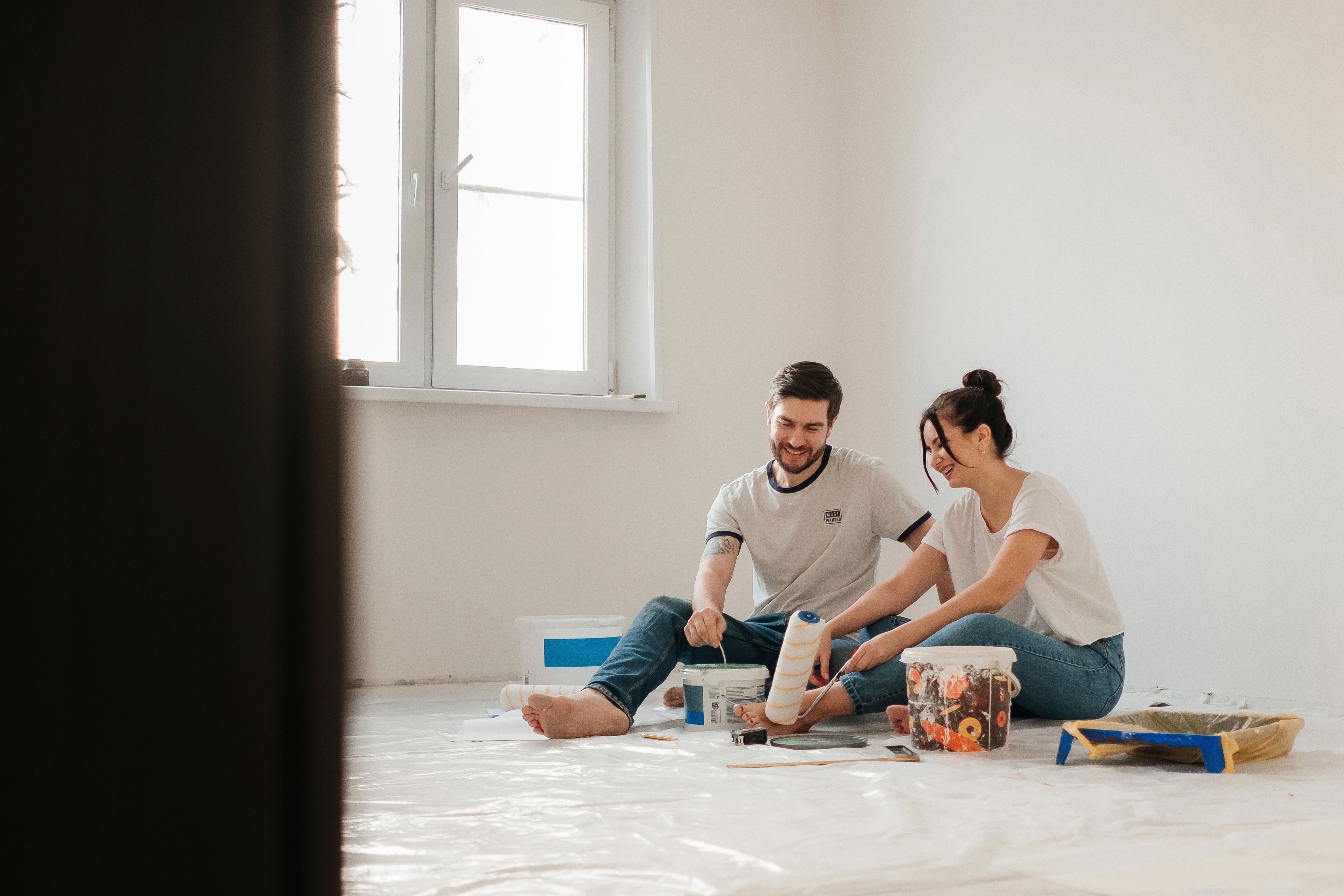Person painting a white wall with a roller in a bright room